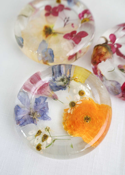 Resin Trinket Dish with clear resin and embedded colorful dried flowers, including a vivid orange bloom and blue petals.